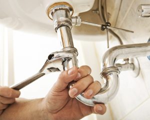 Plumber using a wrench to tighten a siphon under a sink. (iStock)